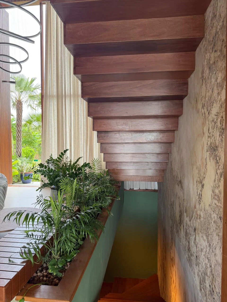 Parte inferior dos degraus de uma escada de madeira ao lado de um jardim interno.